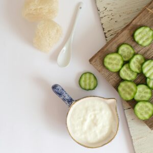 Flat lay of cream in a jug with cucumbers on a wooden board. Perfect for healthy eating themes.