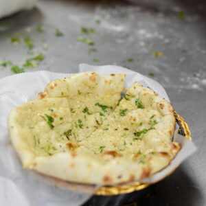 Close-up shot of freshly made garlic naan bread with herbs on a kitchen surface.