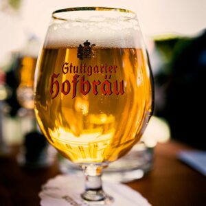 A Stuttgarter Hofbräu beer glass filled with beer on a coaster with a blurred background.