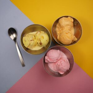 Vibrant ice cream scoops in metal bowls on colorful background.