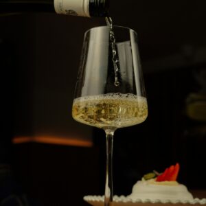 Chilled white wine elegantly poured into a glass with a dessert in the background