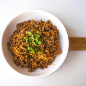 A flavorful bowl of seasoned ground beef garnished with cheese and green onions.