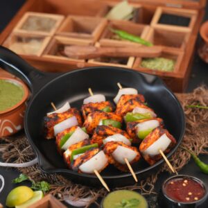 Appetizing grilled paneer tikka in skillet with chutneys