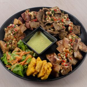 Assorted grilled meats with fresh salad and dip on a black plate.