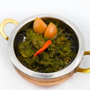 Close-up of spicy Indian saag dish garnished with chili in a traditional brass bowl.