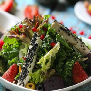 A colorful mixed green salad with strawberries and sesame cheese
