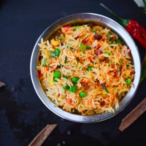 Top view of colorful biryani with vegetables in a metal bowl